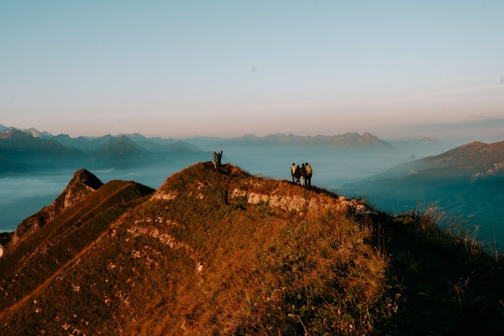 a hill with people standing at the crest looking at the horizon